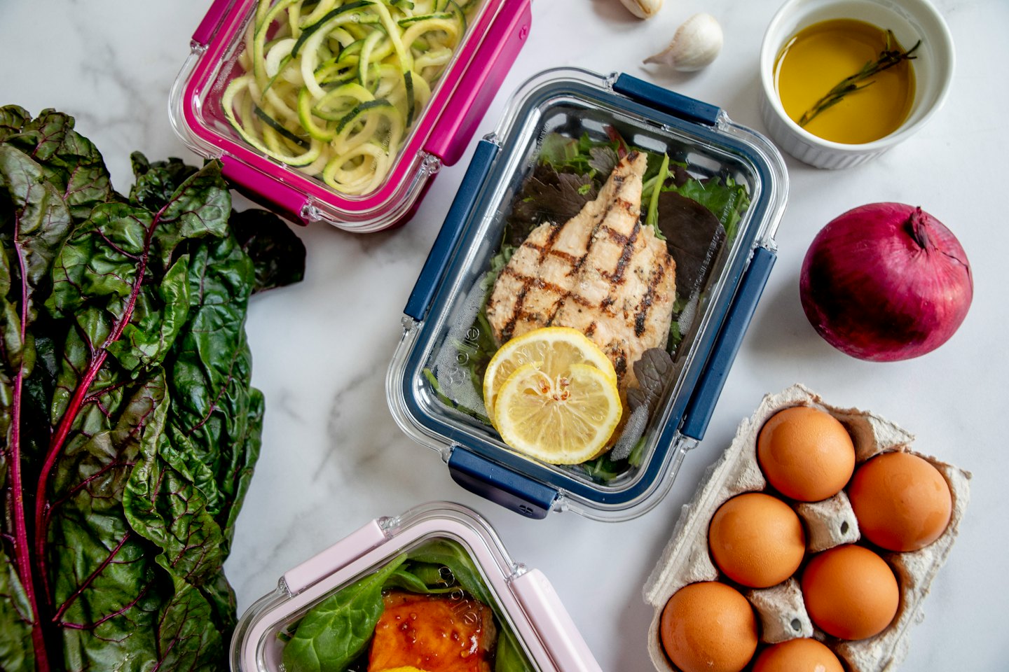 Tre contenitori per meal prep con cibo sano su un bancone di marmo bianco.